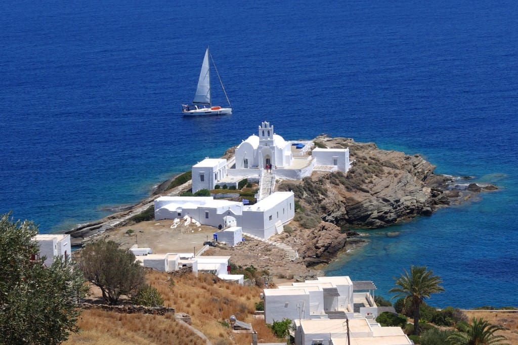 Panagia Chrysopigi monastery on its rocky islet with sailboat and hillside houses in Sifnos